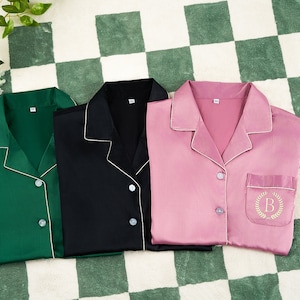 May include: Three satin pajamas in green, black, and pink with white piping. The pink pajamas have a pocket with an embroidered letter "B" on the left side.
