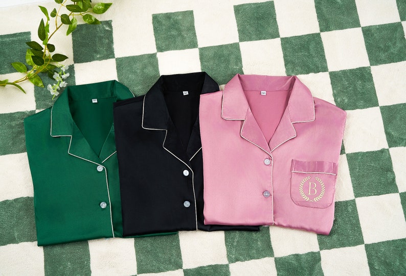 May include: Three satin pajamas in green, black, and pink with white piping. The pink pajamas have a pocket with an embroidered letter "B" on the left side.