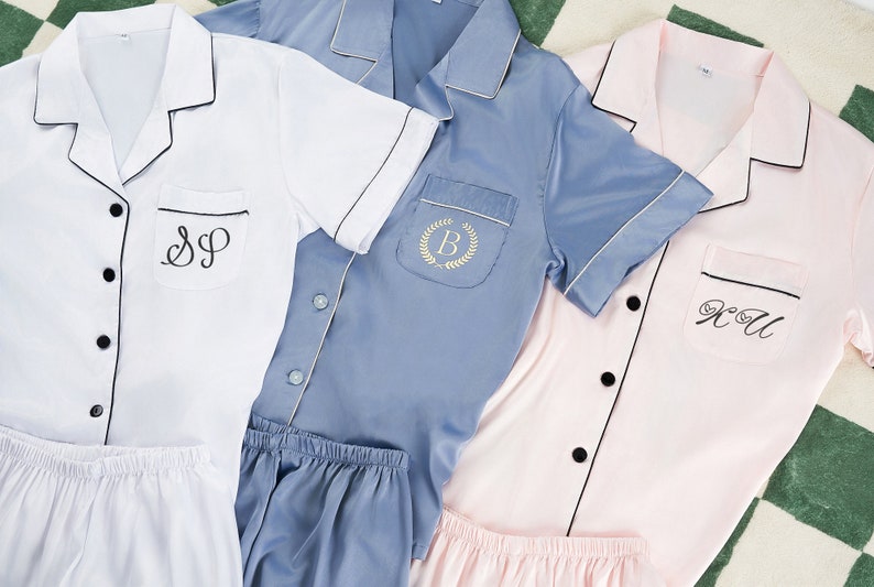May include: Three short-sleeved pajamas with black piping and personalized embroidery. The pajamas are in white, light blue, and pink.