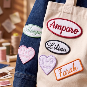 May include: A dark blue denim jacket and a cream canvas tote bag decorated with embroidered patches. The patches feature names including Maryse, Amparo, Lilian, and Farah, along with heart-shaped patches displaying initials H+C and Y+P with dates.