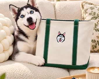 Può includere: Una borsa tote in tela color crema con manici e base verde scuro, caratterizzata da una toppa ricamata raffigurante il muso di un cane husky sul davanti. La borsa è posizionata accanto a un cane husky dal pelo nero, bianco e grigio.