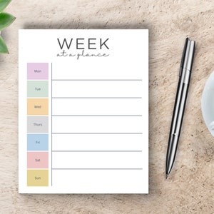 May include: A white weekly planner with the text "WEEK at a glance" at the top. The planner has a column for each day of the week, with a colored box next to each day's name. The colors are purple, green, yellow, gray, blue, pink, and yellow.