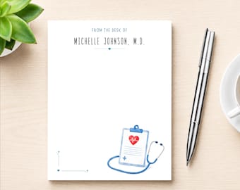 May include: A white notepad featuring the text FROM THE DESK OF MICHELLE JOHNSON, M.D. in blue ink. The design includes a small blue heart, a watercolor illustration of a medical clipboard with a red heart, and a blue stethoscope at the bottom.