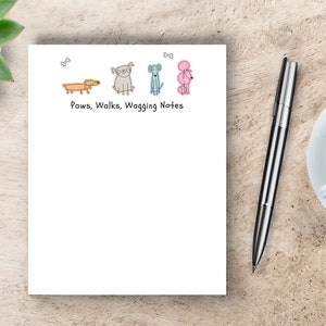 May include: A white notepad with a line of three cartoon dogs and the text "Paws, Walks, Wagging Notes".