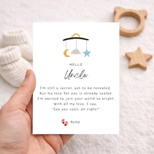 May include: A greeting card with the words "Hello Uncle" and a poem about a new baby. The card features a mobile illustration with a moon, cloud, and star. Beside the card are baby booties, a wooden bear-shaped teether, and a wooden star.