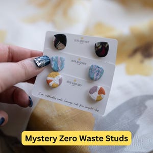 May include: Three pairs of colorful, handmade clay earrings on a white card with the text "SUN AND SKY" and "I am sustainably made Earrings made from recycled clay".