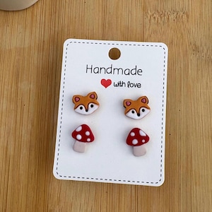 Op de afbeelding: Een set van vier handgemaakte polymer clay oorbellen met een vos- en paddenstoelontwerp. De oorbellen worden getoond op een witte kaart met de tekst "Handmade with love".