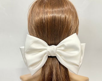 May include: A large white satin bow hair clip. The bow is tied in a classic shape with two large loops and a center knot.