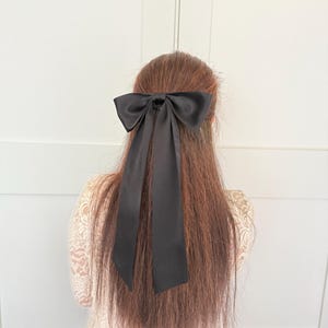 Könnte beinhalten: Ein schwarzes Satinband, das zu einer Schleife gebunden ist, mit langen Bändern. Die Schleife ist in einem einfachen Knoten gebunden und die Bänder hängen am Hinterkopf herunter.