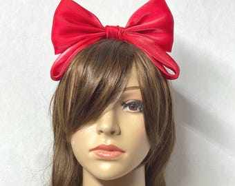 May include: A large, bright red satin bow headband. The bow is tied in a large, full knot and the headband is made of a thin, flexible material.