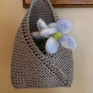 May include: A gray knitted hanging planter with a light blue and white felt flower inside.