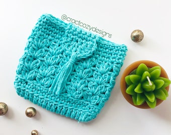 Può includere: Pochette all'uncinetto turchese con nappa, caratterizzata da un motivo a punto strutturato. La borsa fatta a mano è esposta con una piccola candela a succulenta e sfere dorate, creando un'estetica accogliente.