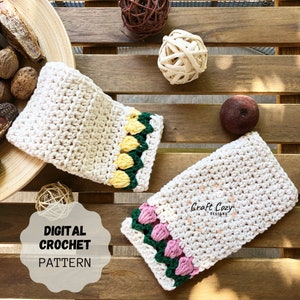 May include: Two crochet dishcloths with a textured stitch pattern. One dishcloth has a yellow and green border with yellow flower accents. The other dishcloth has a pink and green border with pink flower accents. The dishcloths are on a wooden surface. The text "Craft Cozy Designs" is visible on the dishcloth with the pink flower accents.