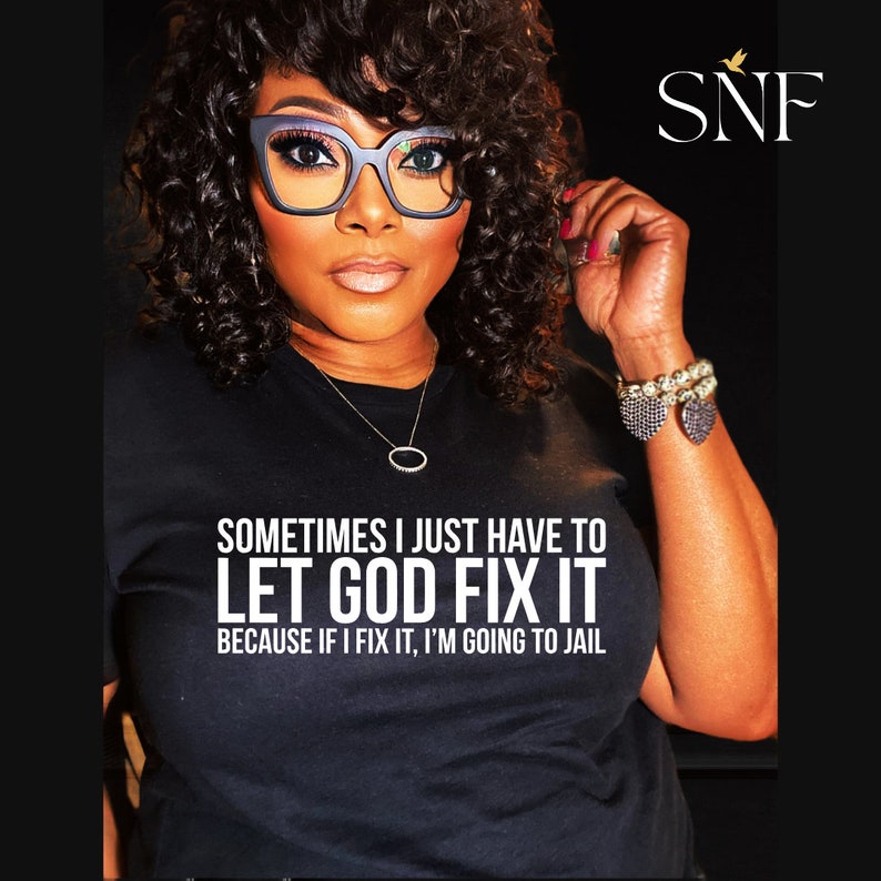 May include: A woman wearing a black t-shirt with the text "Sometimes I just have to let God fix it because if I fix it, I'm going to jail." The woman is wearing glasses and a necklace. The text "SNF" is in the upper right corner of the image.