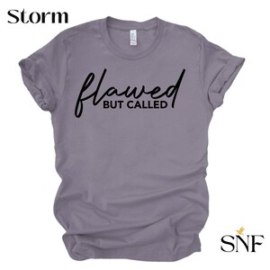 May include: A purple t-shirt with the text "flawed but called" in black script.