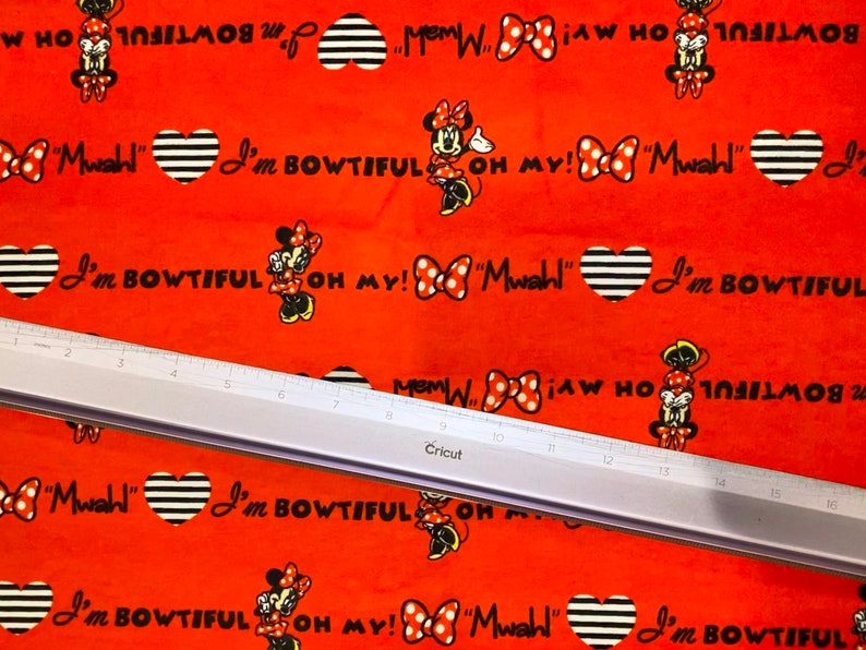 May include: Red fabric with a repeating pattern of a cartoon mouse character with black and white striped hearts, bows, and the text "I'm Bowtiful" and "Oh My!"  "Mwahl!"