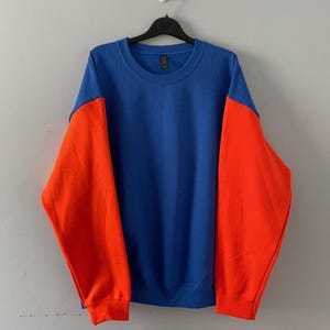 May include: A blue and orange sweatshirt with long sleeves. The sleeves are orange and the body of the sweatshirt is blue.