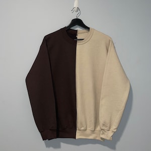 May include: A brown and beige sweatshirt with a vertical split down the middle. The left side is brown and the right side is beige.