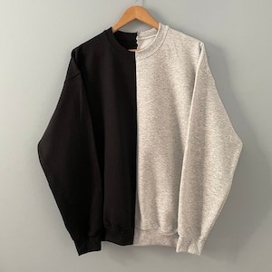 May include: A black and grey sweatshirt with a vertical seam down the center, creating a split design.