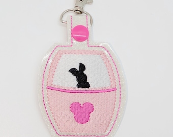 May include: Pink and white glitter keychain with a pink Mickey Mouse head and a black silhouette of a ride vehicle.