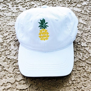 May include: White baseball cap with an embroidered pineapple design. The pineapple is made up of yellow Mickey Mouse heads with green leaves.
