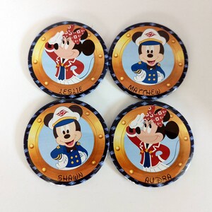 May include: Four round, colorful, pin-back buttons featuring Disney characters dressed as cruise ship captains. The buttons have gold trim and the names "Leslie", "Matthew", "Shawn", and "Audra" printed on them.