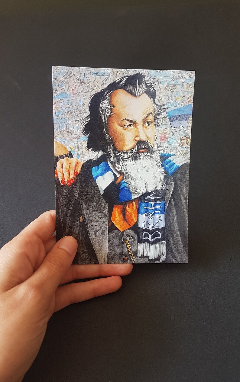 Puede incluir: Una postal con un retrato detallado de un hombre con barba y bigote largos y blancos, que lleva un abrigo negro, una corbata naranja y una bufanda azul y blanca. El fondo muestra una multitud. La postal es sostenida por una mano.