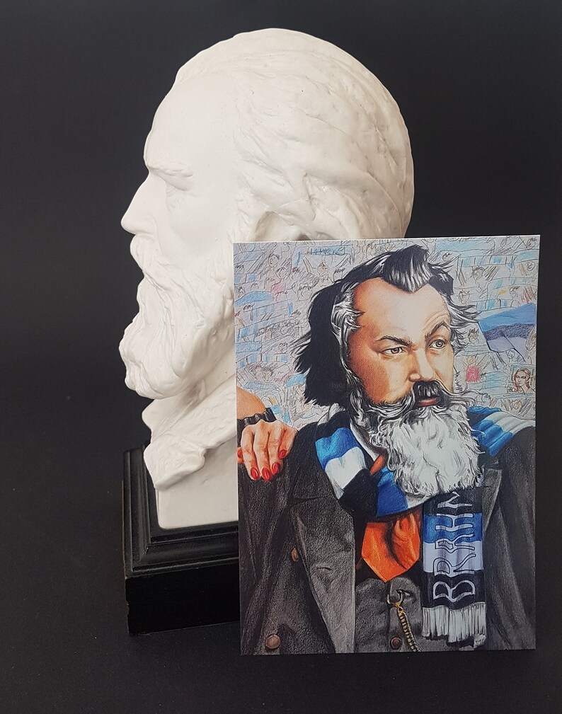 Puede incluir: Un busto de yeso blanco de un hombre con barba larga est&aacute; junto a una postal. La postal presenta un retrato a l&aacute;piz de color de un hombre barbudo, con una bufanda a rayas azules y blancas con la palabra "BRKN".
