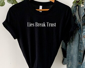 May include: Black t-shirt with the text "Lies Break Trust" printed in white on the front. The t-shirt is hanging on a rack with a denim jacket.