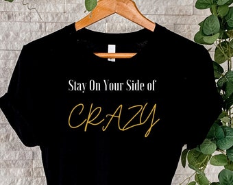 May include: Black t-shirt with the text "Stay On Your Side of Crazy" in white and gold lettering.