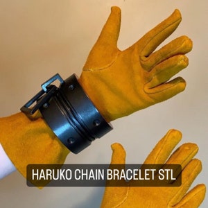 May include: A pair of yellow leather gloves with a black metal chain bracelet on one wrist. The bracelet has a series of interlocking rings and is labeled "HARUKO CHAIN BRACELET STL".