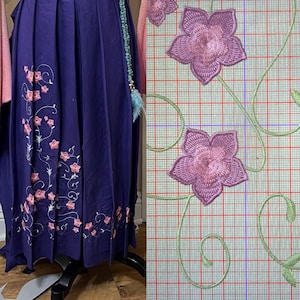 May include: A long, dark blue skirt with pink floral embroidery along the hem and side. The embroidery features delicate pink flowers and green vines. The skirt is displayed on a black dress form.