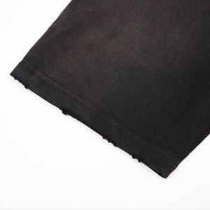 May include: A black fabric sleeve featuring a straight hemline with a distressed, frayed edge. The garment is constructed with double-needle stitching along the cuff, providing a clean finish above the intentionally worn and textured raw edge.