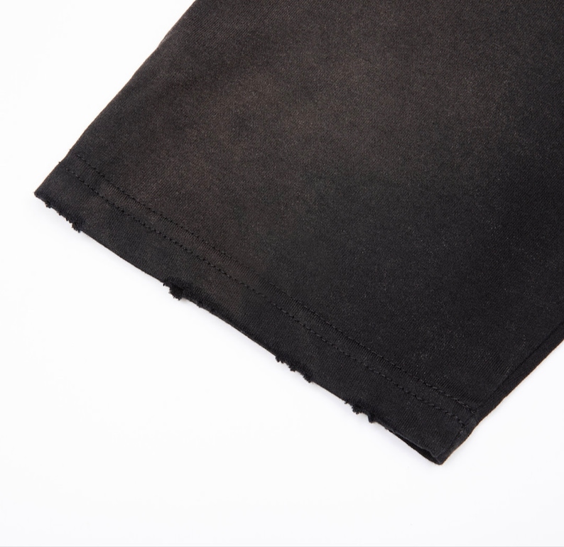 May include: A black fabric sleeve featuring a straight hemline with a distressed, frayed edge. The garment is constructed with double-needle stitching along the cuff, providing a clean finish above the intentionally worn and textured raw edge.