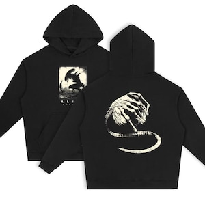 May include: Black hooded sweatshirt featuring a graphic from the movie "Alien". The front displays a scene with the word "ALI" at the bottom. The back of the sweatshirt shows a detailed illustration of the alien creature. The design is in white against a black background.