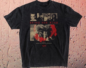 May include: A black t-shirt featuring a movie poster design. The graphic includes the text "BRING HER BACK" in white, with images of faces and a red and beige graphic. The shirt is a dark, faded color.