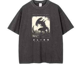 May include: A black t-shirt with a vintage-style graphic of the Alien creature from the movie "Alien." The graphic is in white and features the text "There's something in the water" and "Alien Romulus."