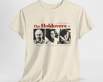 May include: A beige t-shirt with a black and white image of three actors from the movie "The Holdovers". The movie title is in red text with the rating "R" next to it. The actors' names are listed below their images.
