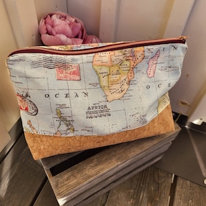 Peut inclure: Une pochette zippée bleue et marron avec un fond en liège. La pochette présente un imprimé de carte du monde vintage avec le texte "OCEAN" et "MAP OF AFRICA".