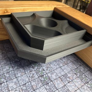 May include: A black plastic tray with multiple compartments for dice and other gaming accessories. The tray is attached to a wooden gaming table.