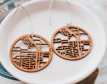 May include: A pair of wooden earrings shaped like a city map. The earrings are brown and have a silver hook.