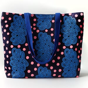 Puede incluir: Un bolso tote con fondo azul marino, lunares rosas y formas abstractas azules. El bolso tiene asas azules y est&aacute; hecho de tela. El bolso tote es un accesorio elegante para llevar objetos.