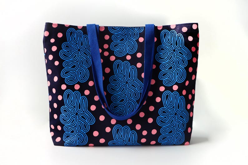 Puede incluir: Un bolso tote con fondo azul marino, lunares rosas y formas abstractas azules. El bolso tiene asas azules y est&aacute; hecho de tela. El bolso tote es un accesorio elegante para llevar objetos.
