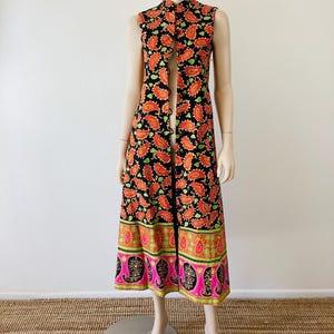 May include: A long, black sleeveless dress with a paisley print in shades of orange, green, and pink. The dress has a mandarin collar and a front opening with buttons.