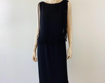 May include: Black sleeveless dress with a pleated top and a straight skirt. The top features vertical pleats and thin, dangling straps. The dress is displayed on a mannequin against a plain white background. A classic, elegant design.