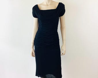 May include: A black dress with a square neckline and short sleeves. The dress features a ruched bodice and a knee-length skirt. The dress is displayed on a mannequin against a white background. The dress is made of a soft, flowing fabric.