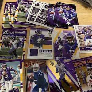 May include: A collection of trading cards featuring a football player in a purple and gold uniform. The cards are from different sets and feature different designs. The text on the cards includes "Teddy Bridgewater", "Donruss Threads", "Goodwin Champio", "Score", "Gridiron Kings", and "Vikings".