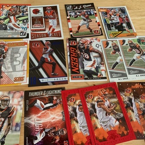 May include: A collection of trading cards featuring American football player A.J. Green. The cards are from different sets and feature various designs, including a red and black card with the text "Thunder & Lightning" and a red card with the text "Classics".