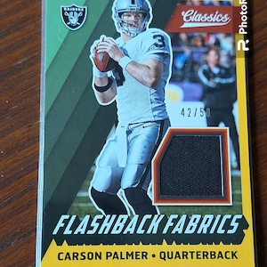 May include: A football card featuring Carson Palmer, a quarterback for the Raiders. The card is from the "Flashback Fabrics" series and is numbered 42/50. The card has a green, yellow, and black color scheme.