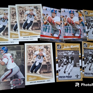 May include: A collection of vintage trading cards featuring Archie Manning, a former NFL quarterback. The cards are in various conditions, some are in mint condition, while others show signs of wear. The cards feature different photos of Manning in his New Orleans Saints uniform.